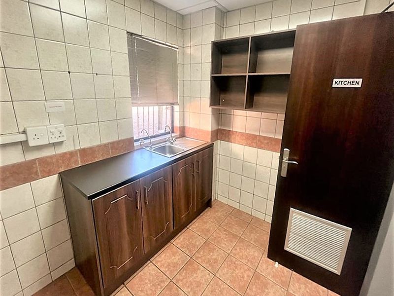 A compact office kitchenette featuring built-in cabinetry, a stainless steel sink, tiled surfaces, and open shelving for storage.