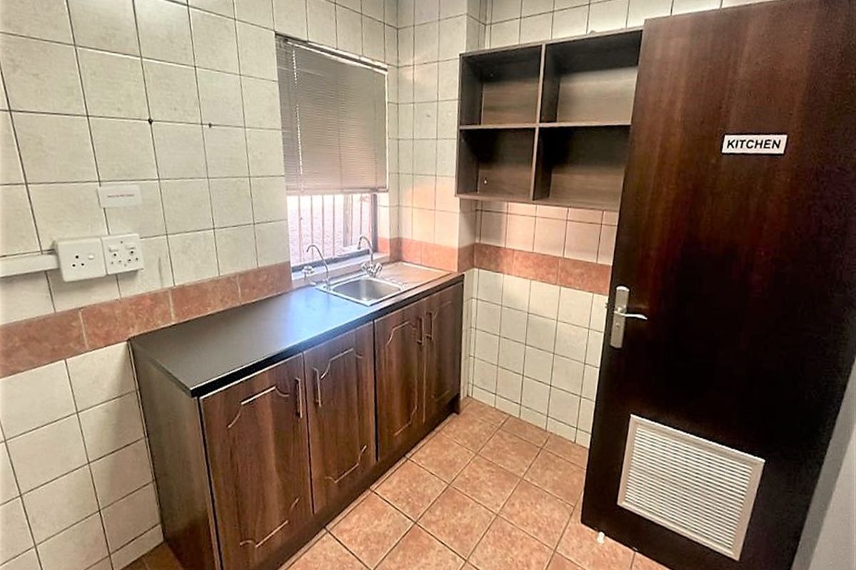 A compact office kitchenette featuring built-in cabinetry, a stainless steel sink, tiled surfaces, and open shelving for storage.