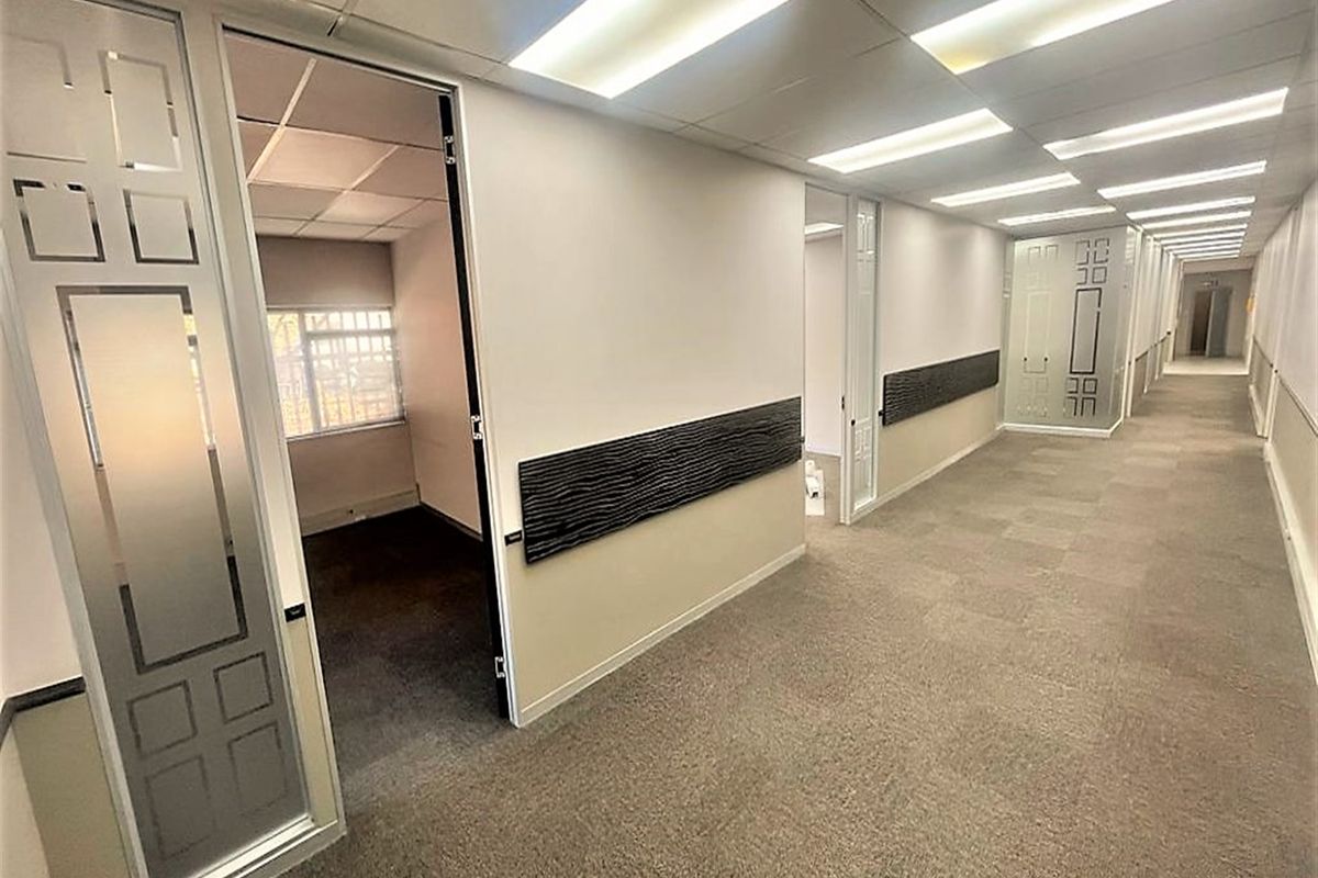 A clean, well-lit office hallway featuring carpeted floors, suspended ceilings, and frosted glass doors leading into individual office spaces.