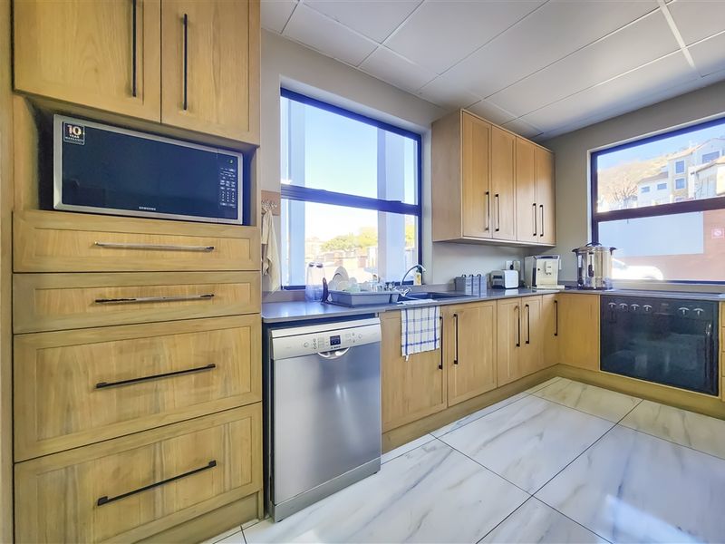 A well-maintained office kitchen featuring light wood cabinetry, integrated appliances, modern tiled flooring, and ample natural light from large windows.