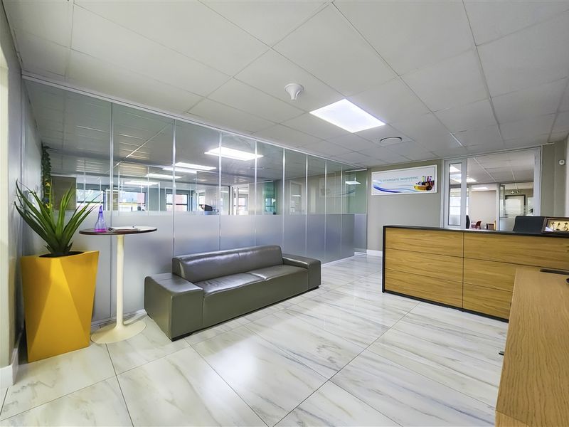 Modern office reception area featuring marble-effect tiled flooring, glass partition walls, and a professional built-in reception desk with recessed ceiling lighting.