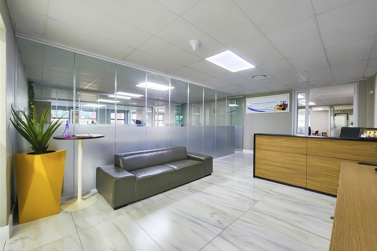 Modern office reception area featuring marble-effect tiled flooring, glass partition walls, and a professional built-in reception desk with recessed ceiling lighting.