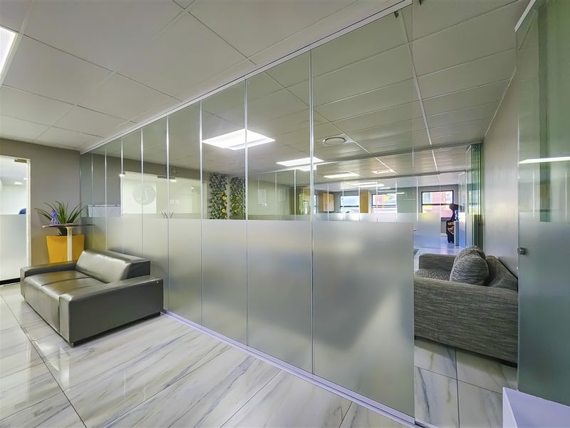 Modern office space featuring a sleek glass partition wall with frosted privacy film, suspended ceiling, and polished tiled flooring.