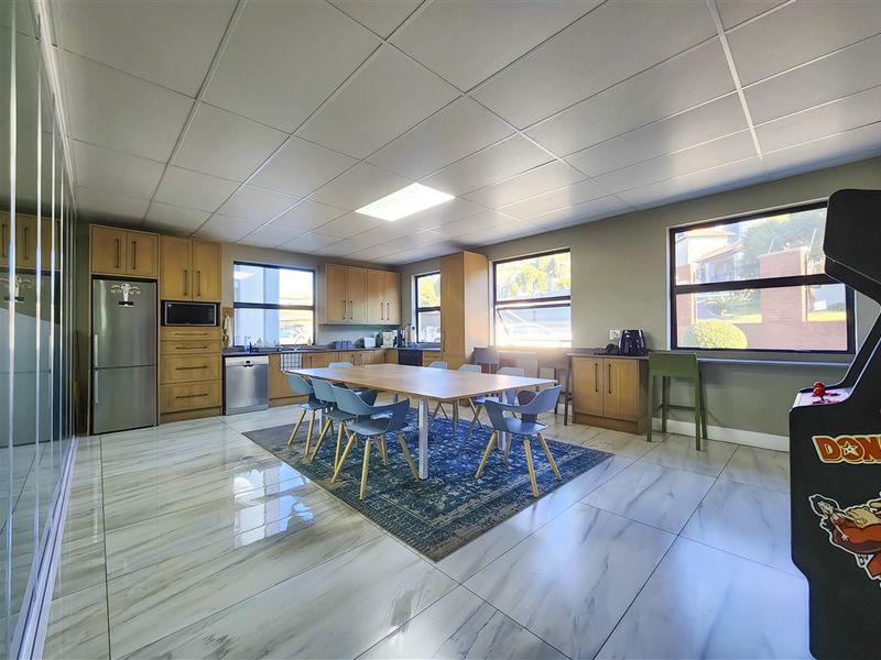 Spacious open-plan office kitchen and dining area featuring modern tiled flooring, ample built-in cabinetry, and large windows providing natural light.