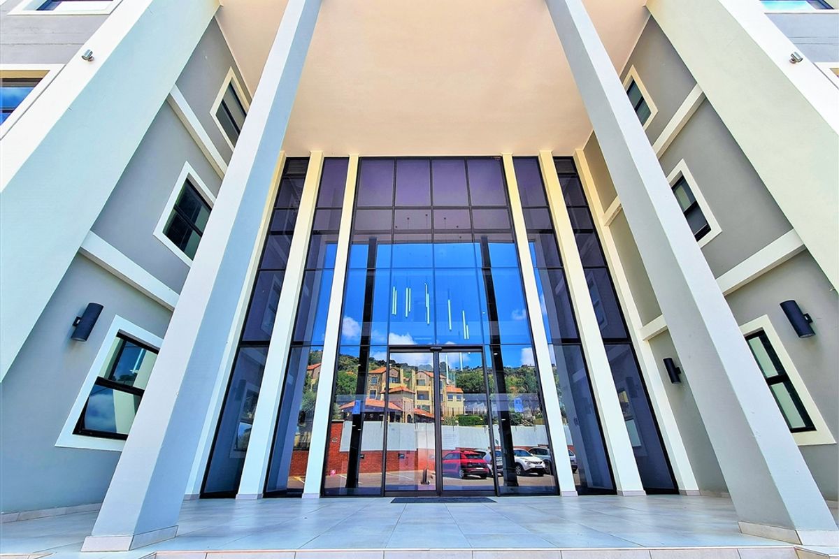 Modern office building entrance featuring a prominent glass facade, structural columns, and a clean tiled porch area.