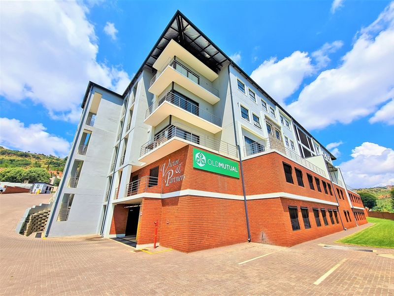 A modern multi-story office building featuring a combination of brick and rendered facade, multiple balconies, and a paved parking area.