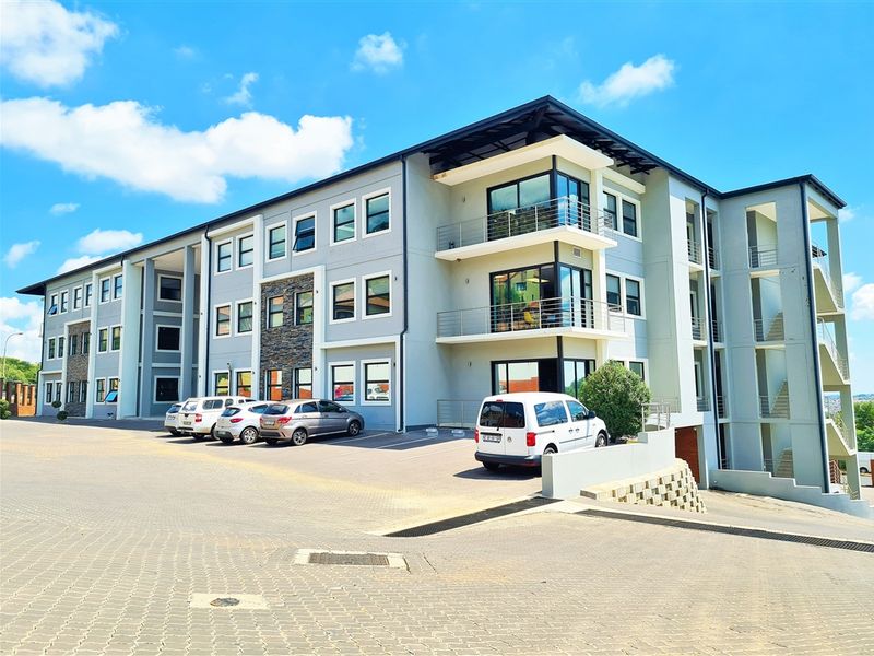 Modern multi-story office building featuring stone cladding, glass-fronted balconies, and an integrated paved parking area.