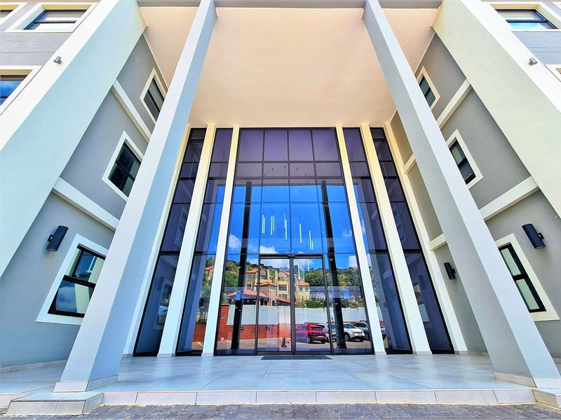 Modern office building entrance featuring a prominent glass facade, structural columns, and a clean tiled porch area.