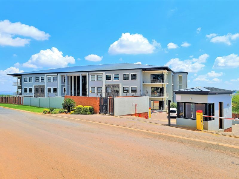 A professional exterior view of a modern office complex featuring a secure gated entrance, guard house, and multi-level building with balconies.