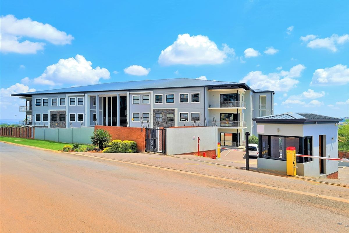 A professional exterior view of a modern office complex featuring a secure gated entrance, guard house, and multi-level building with balconies.