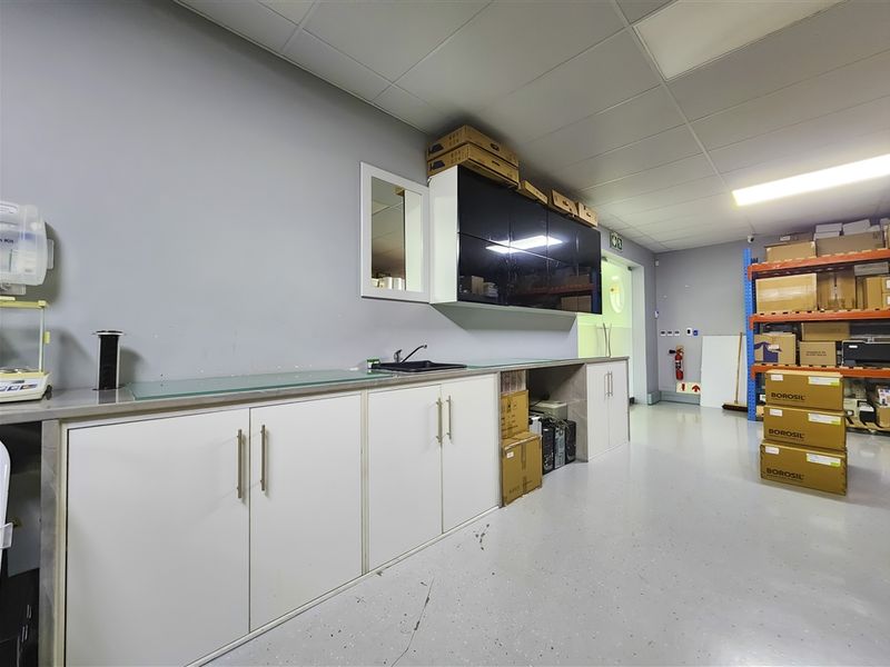 Functional utility space featuring built-in cabinetry, a sink, and durable flooring, suitable for office storage or a staff kitchenette area.