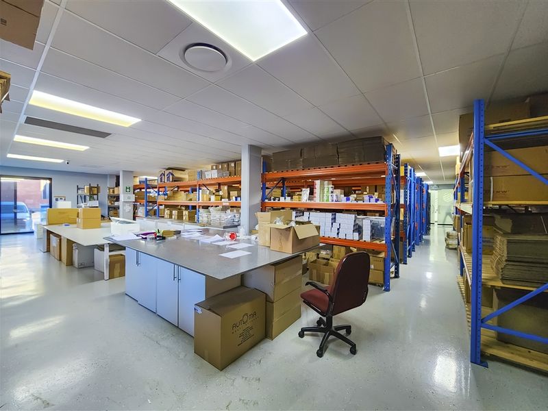 A functional industrial utility and storage space featuring durable epoxy flooring, suspended ceilings with recessed lighting, and extensive built-in steel racking systems.