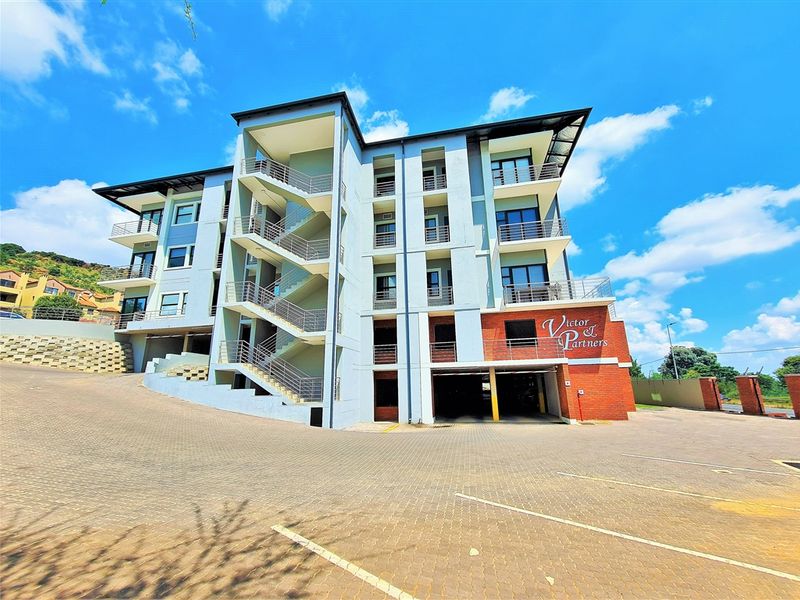 Modern multi-story office building featuring a paved driveway, covered parking area, external staircases, and private balconies.