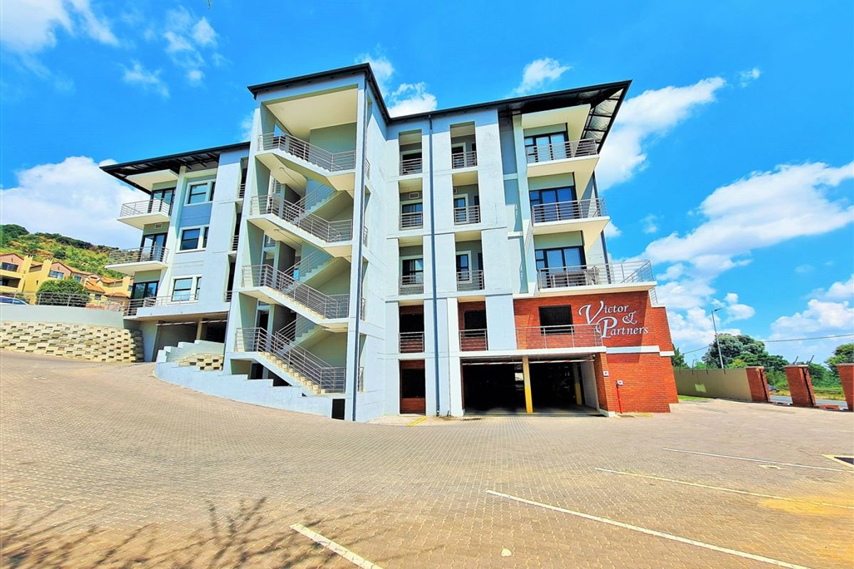 Modern multi-story office building featuring a paved driveway, covered parking area, external staircases, and private balconies.