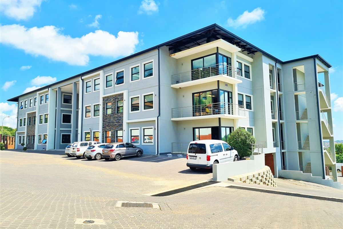 Modern multi-story office building featuring stone cladding, glass-fronted balconies, and an integrated paved parking area.