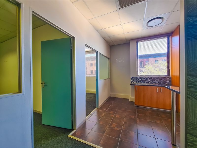 Empty office space featuring a small kitchenette area, suspended ceilings, tiled and carpeted flooring, and internal glass partitions for a professional layout.