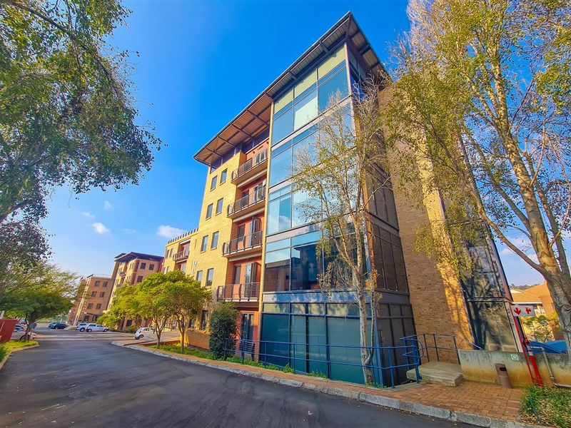 Modern multi-story office building featuring a brick facade, extensive glass curtain walling, and integrated metal balconies with paved access areas.