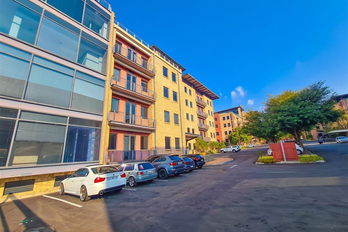 Exterior view of a modern multi-story office building featuring a glass facade, brick exterior, and dedicated parking area.