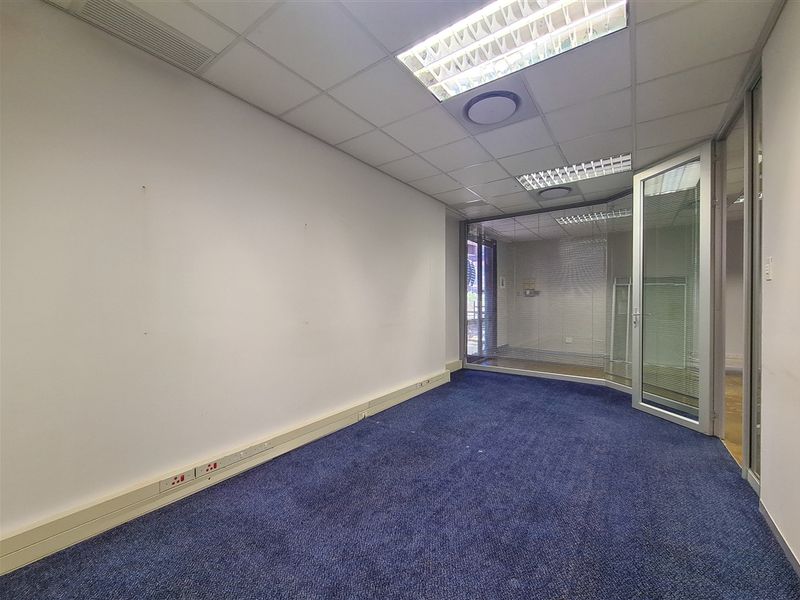 An empty office space featuring a suspended ceiling, recessed lighting, glass partitioning, and blue carpet flooring with integrated electrical trunking.
