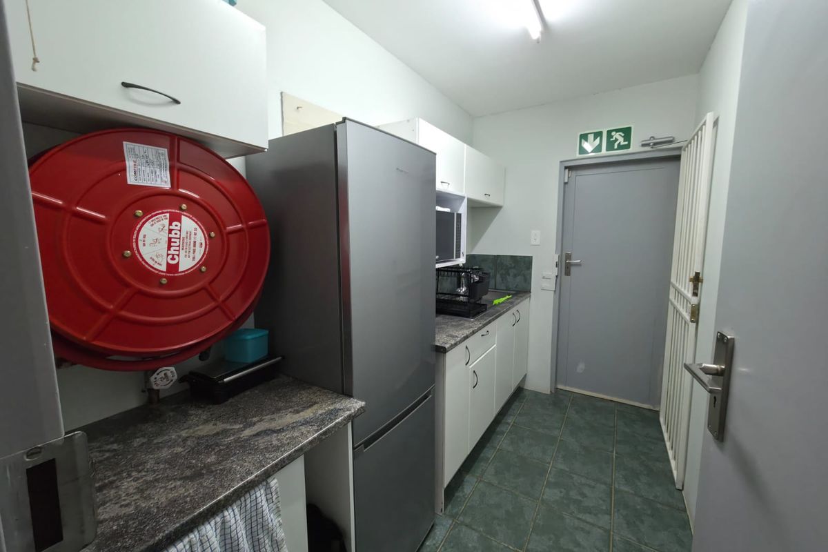 A functional office kitchenette featuring built-in cabinetry, stone-look countertops, tiled flooring, and a wall-mounted fire hose reel.