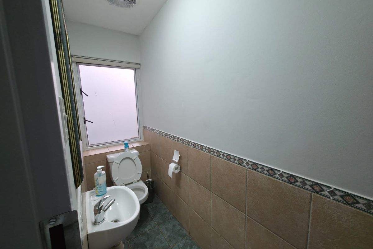 A compact office restroom featuring a pedestal sink, toilet, tiled flooring, and a small window for ventilation.