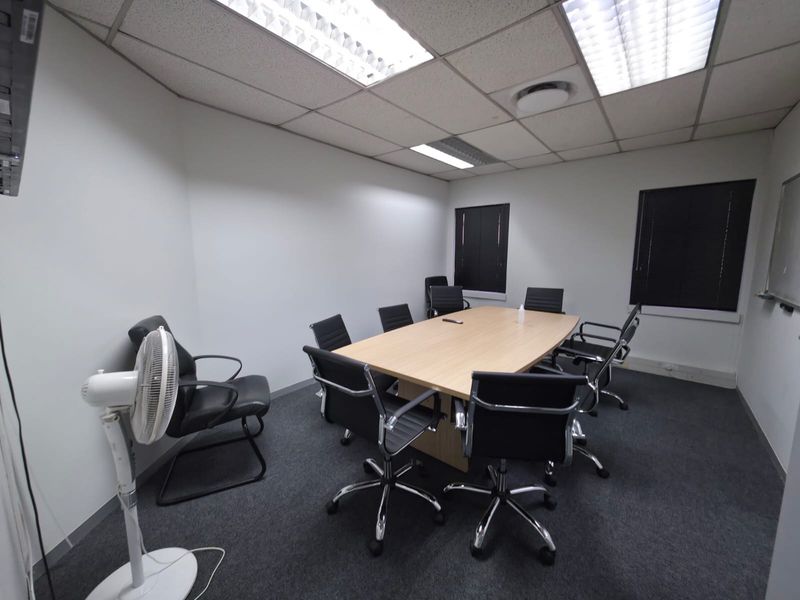 A functional office meeting room featuring a central conference table, suspended acoustic ceiling tiles, and integrated fluorescent lighting.
