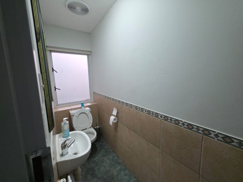 A compact office restroom featuring a pedestal sink, toilet, tiled flooring, and a small window for ventilation.