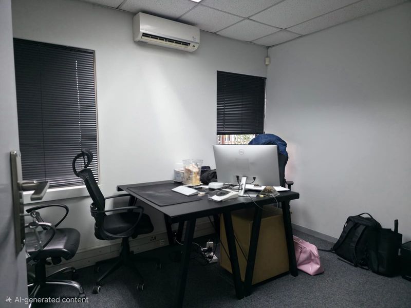 A functional office space featuring a wall-mounted air conditioning unit, suspended ceiling tiles, and window blinds.