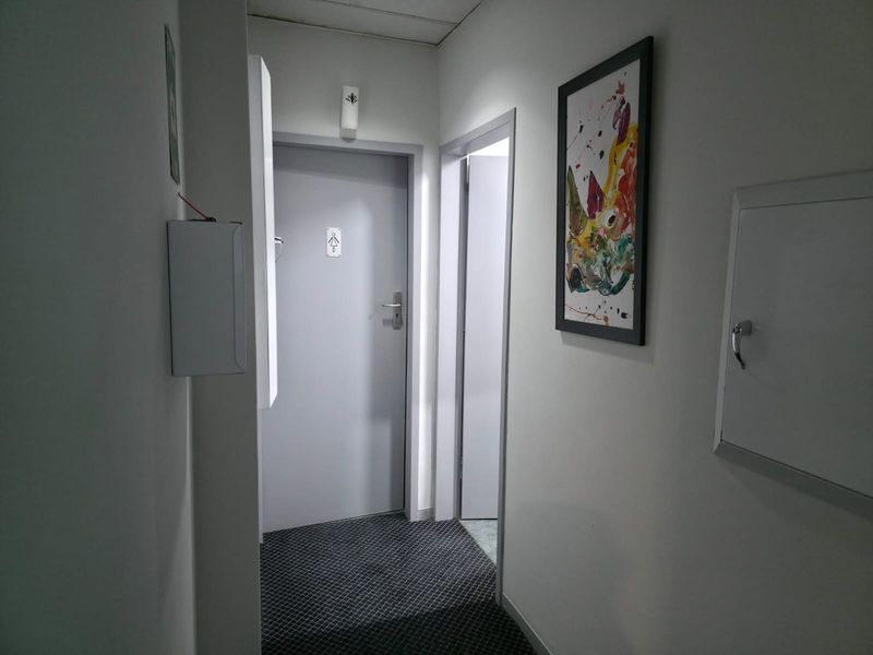 A functional office hallway featuring carpeted flooring, access to restroom facilities, and a wall-mounted utility cabinet.