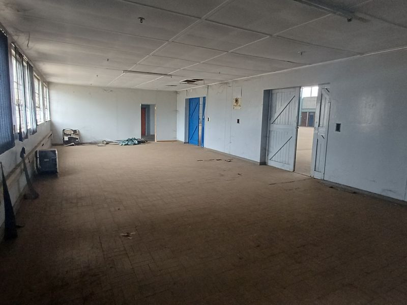 A large, vacant industrial office or utility space featuring worn flooring, suspended ceiling panels, and multiple access doors.