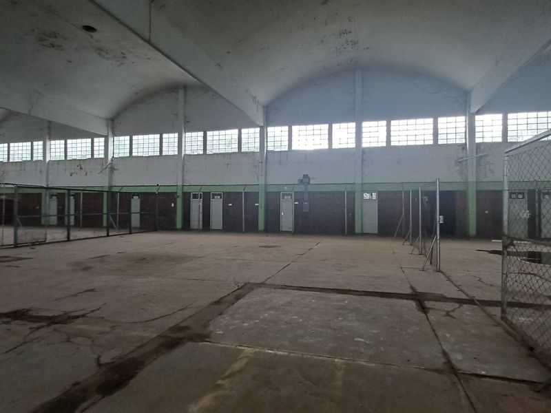 Large industrial warehouse space featuring high vaulted ceilings, clerestory windows, concrete flooring, and internal chain-link fencing partitions.