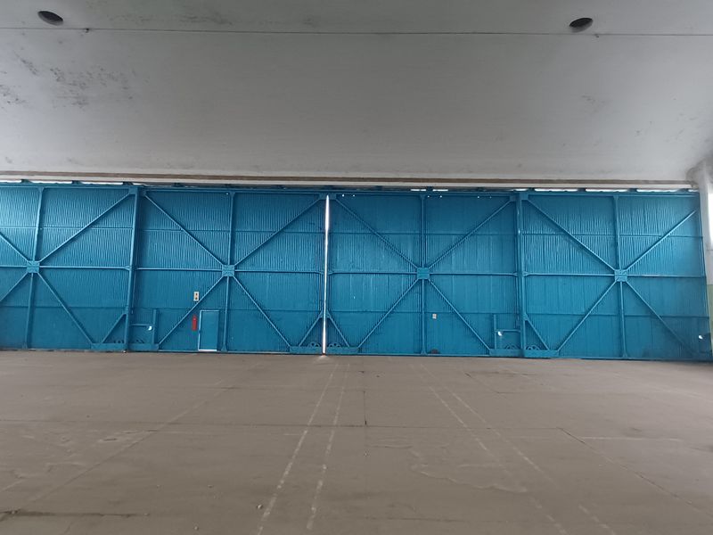 Spacious industrial hangar featuring high vaulted ceilings, large blue sliding metal doors, and expansive concrete flooring suitable for storage or workshop use.
