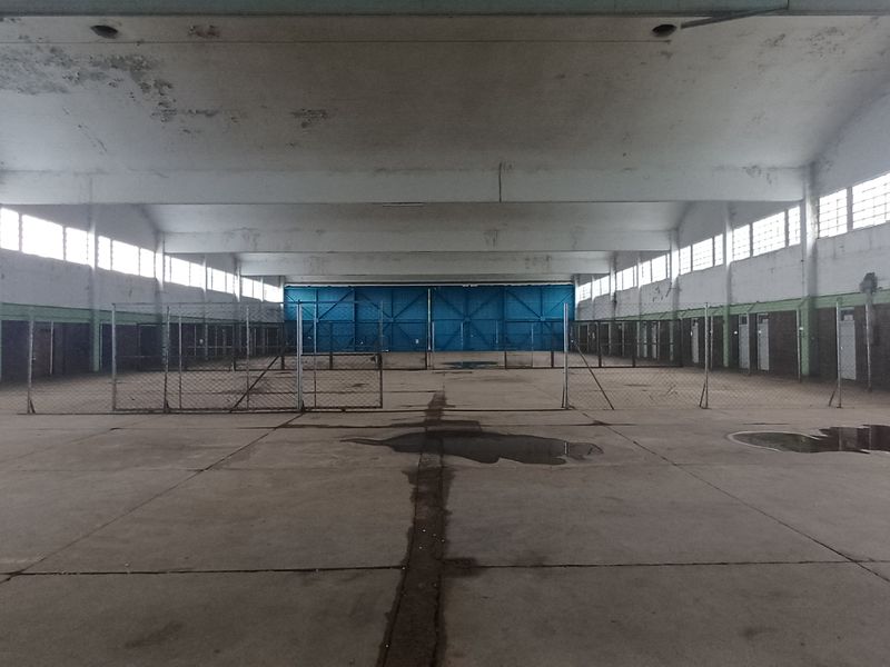Large industrial warehouse space featuring high ceilings, concrete flooring, perimeter chain-link fencing, and multiple access doors.