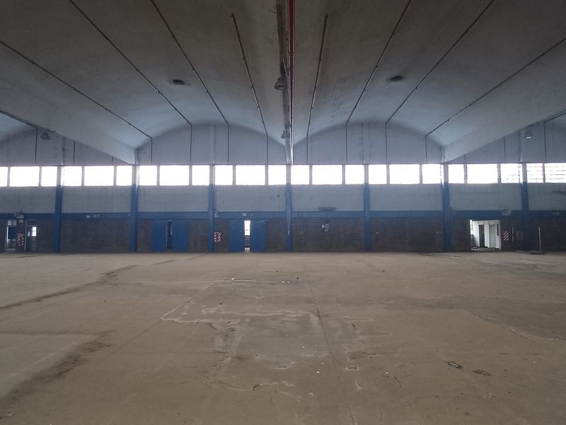 Expansive industrial warehouse space featuring high vaulted ceilings, concrete flooring, and multiple access points, suitable for storage or manufacturing operations.