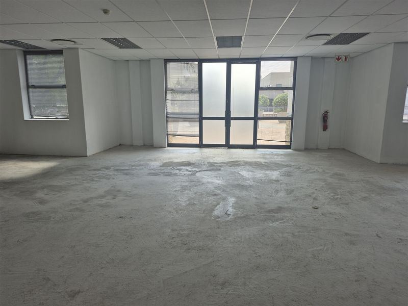 An open-plan office space featuring a suspended ceiling, recessed lighting, and large aluminium-framed windows, currently awaiting final flooring installation.