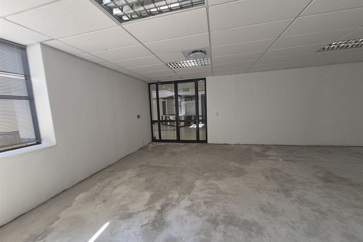 An empty office space featuring a suspended ceiling with recessed lighting, concrete flooring, and an aluminum-framed glass entrance door.
