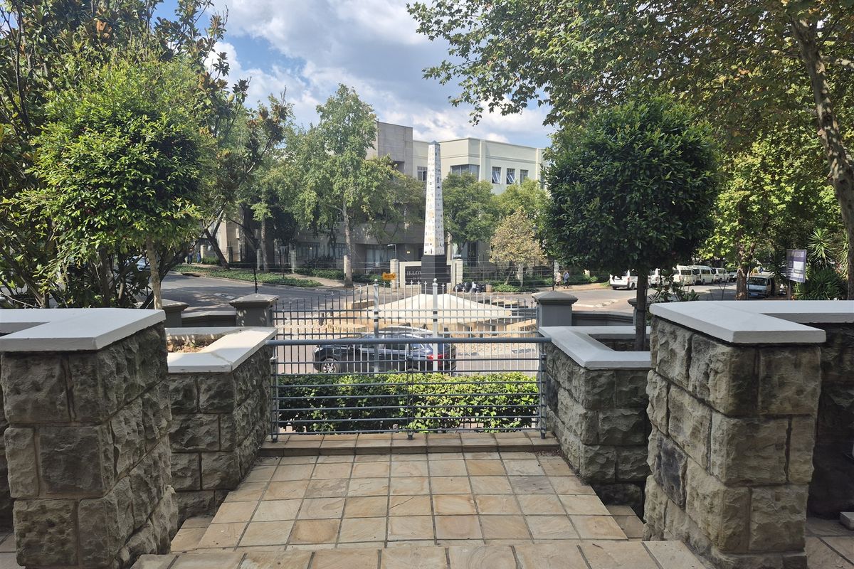 View from the entrance landing overlooking a landscaped street area with stone pillars and metal security fencing.
