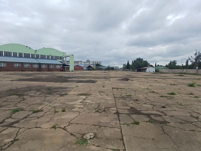Expansive industrial yard featuring a large concrete paved area with significant surface cracking and adjacent industrial warehouse structures.