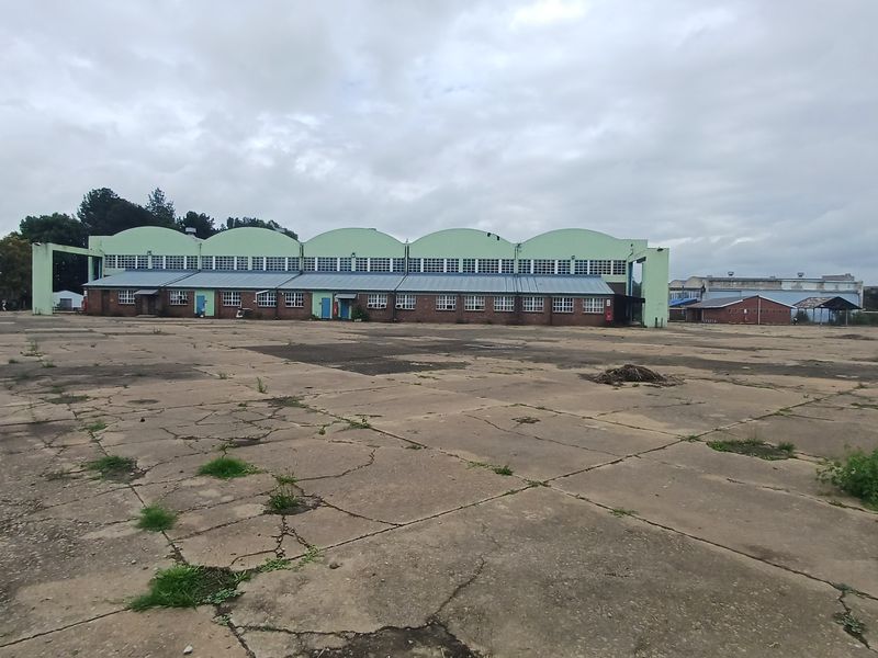 Large industrial warehouse facility featuring a distinctive arched roof design and extensive concrete yard space, suitable for logistics or manufacturing operations.