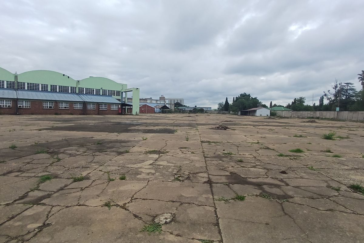 Expansive industrial yard featuring a large concrete paved area with significant surface cracking and adjacent industrial warehouse structures.