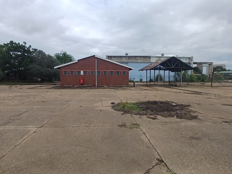 Industrial site featuring a brick building, an open-sided metal structure, and extensive concrete yard space, suitable for redevelopment or storage.