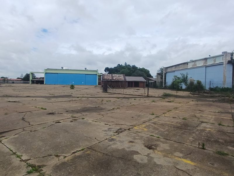 Expansive industrial yard featuring large hangar-style structures, extensive concrete paving, and a small auxiliary building on a spacious site.