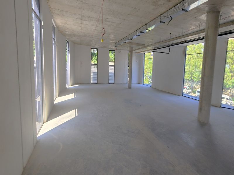 A spacious, open-plan office shell featuring exposed concrete ceilings, polished concrete floors, and large windows providing ample natural light.