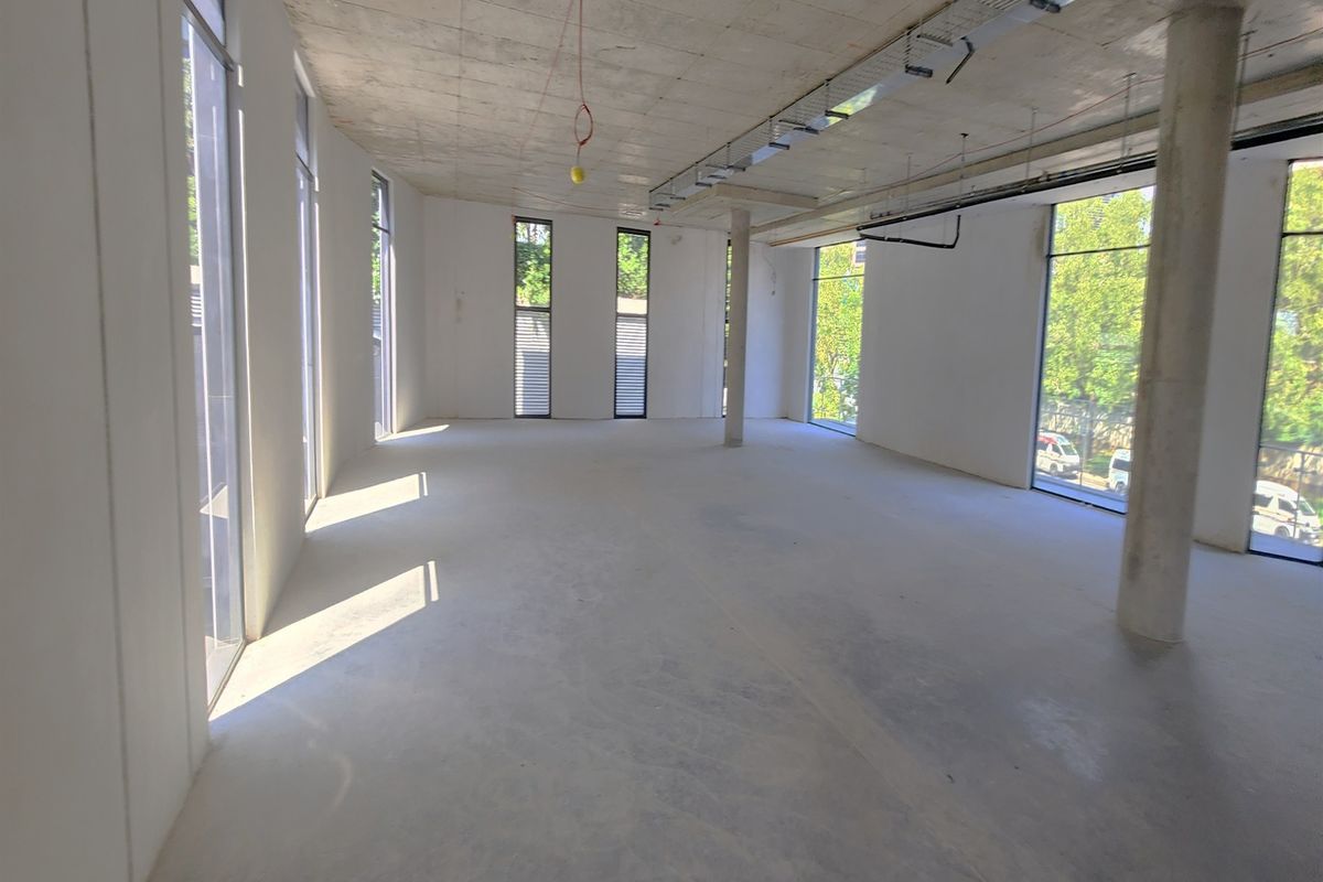 A spacious, open-plan office shell featuring exposed concrete ceilings, polished concrete floors, and large windows providing ample natural light.
