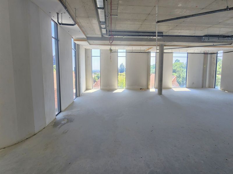 An open-plan office space in shell condition, featuring exposed concrete ceilings, floor-to-ceiling windows, and natural light, ready for custom fit-out.
