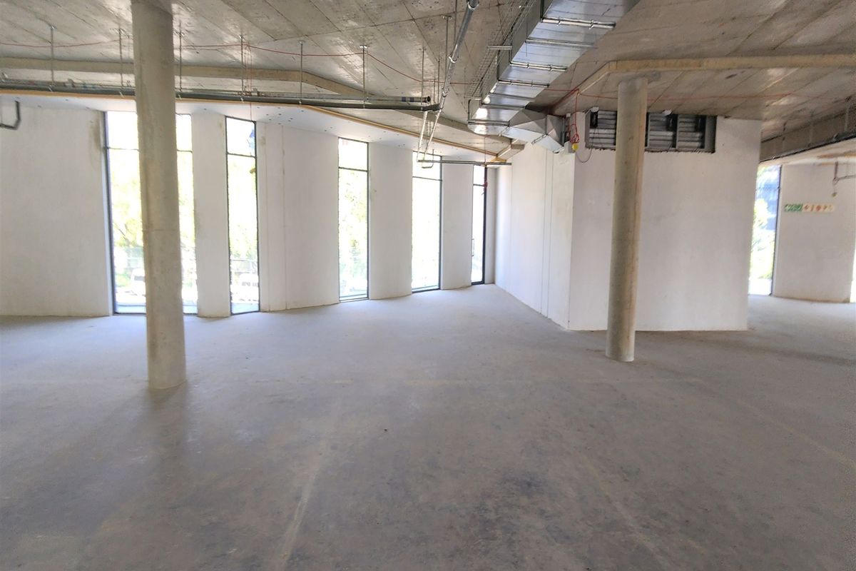 An expansive, open-plan office space in shell condition, featuring exposed concrete ceilings, support columns, and large windows providing ample natural light.