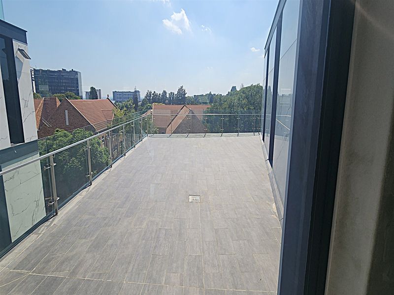 A spacious modern balcony featuring high-quality tiled flooring, a sleek glass balustrade, and expansive glass sliding doors offering an elevated urban view.