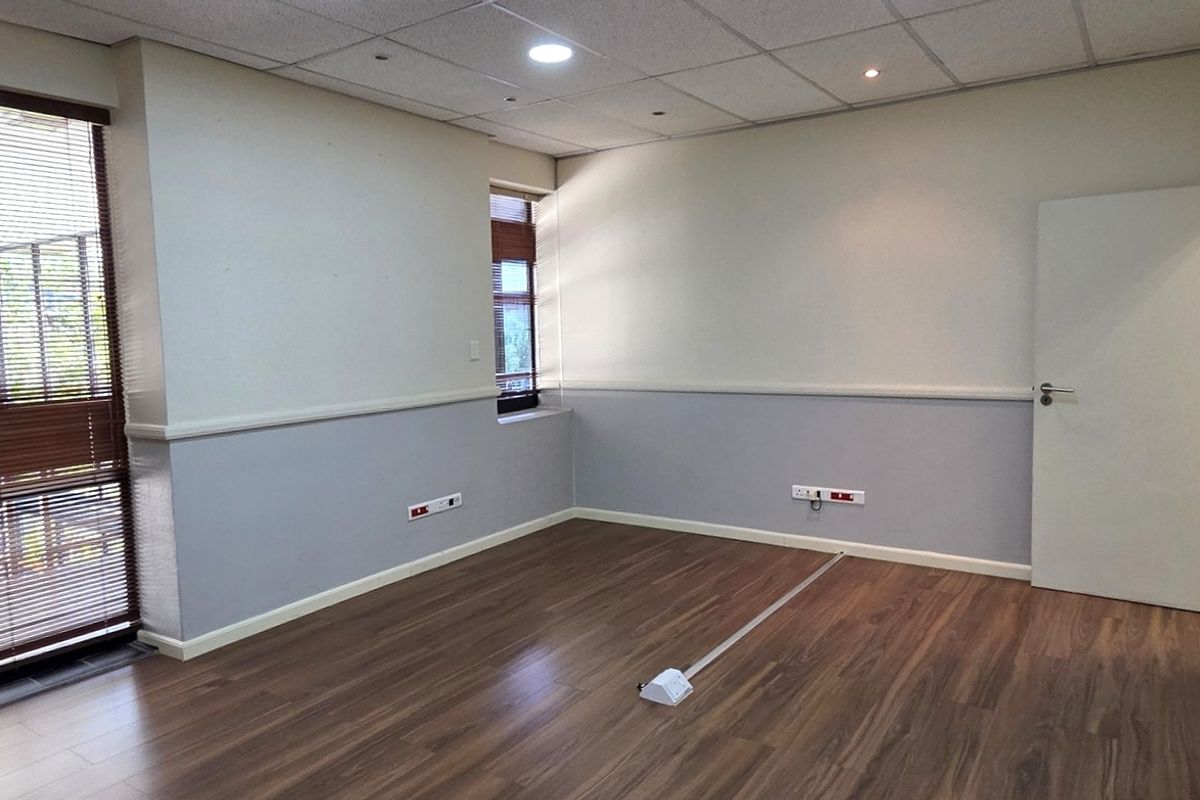 A clean, empty office space featuring laminate flooring, a suspended ceiling with recessed lighting, and large windows with fitted venetian blinds.