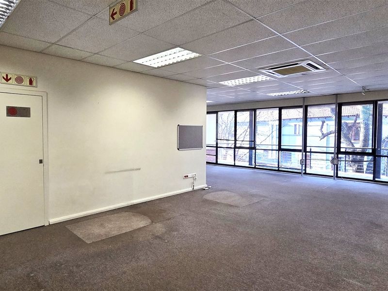 Spacious open-plan office area featuring large windows, suspended ceilings with recessed lighting, integrated air conditioning, and a dedicated storage room.