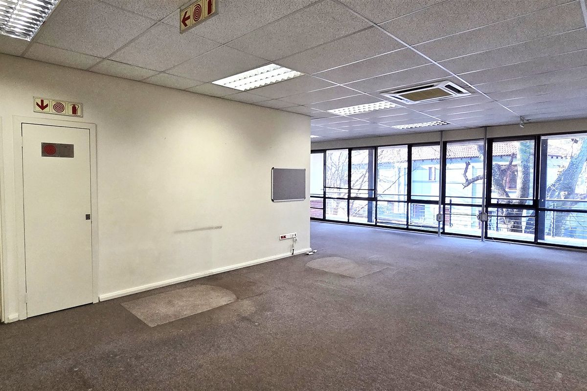 Spacious open-plan office area featuring large windows, suspended ceilings with recessed lighting, integrated air conditioning, and a dedicated storage room.